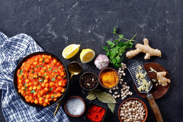 Chana masala indio o curry de garbanzos con ingredientes sobre un fondo de hormigón oscuro