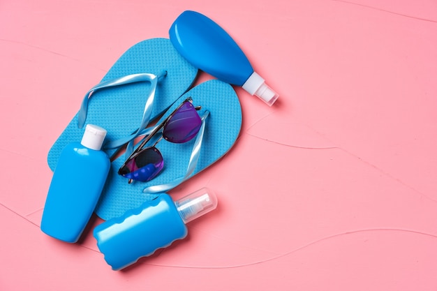 Chanclas azules con protector solar y gafas de sol en rosa, plano