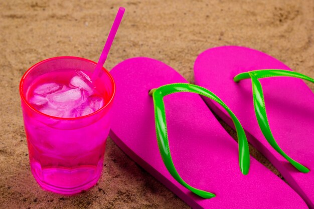 Chanclas y bebida fría con hielo en una playa de arena