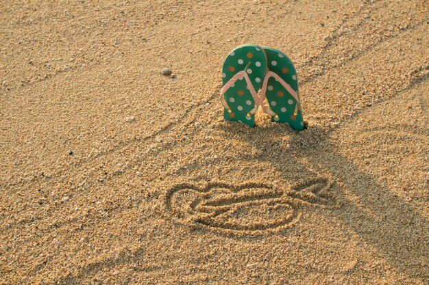 Chanclas coloridas y forma de corazón en la playa de arena blanca en estilo vintage