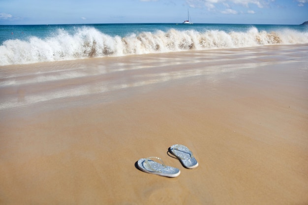 Chanclas plateadas en una playa de arena cerca de una ola