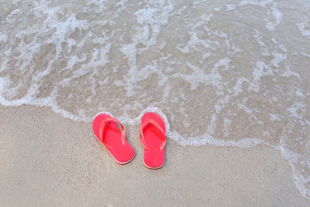 Chanclas en la playa con mar de olas de arena en el mar