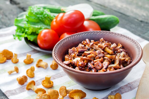 Chanterelles fritos com cebola em uma tigela rústica e prato com legumes frescos para salada na superfície