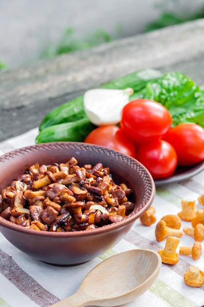 Chanterelles fritos com cebola em uma tigela rústica e prato com legumes frescos para salada