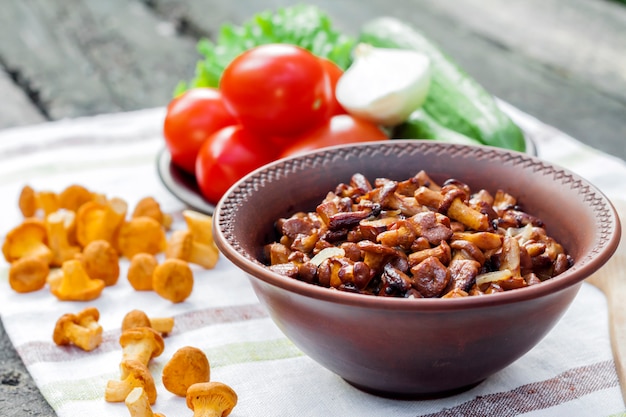 Chanterelles fritos com cebola em uma tigela rústica e prato com legumes frescos para salada