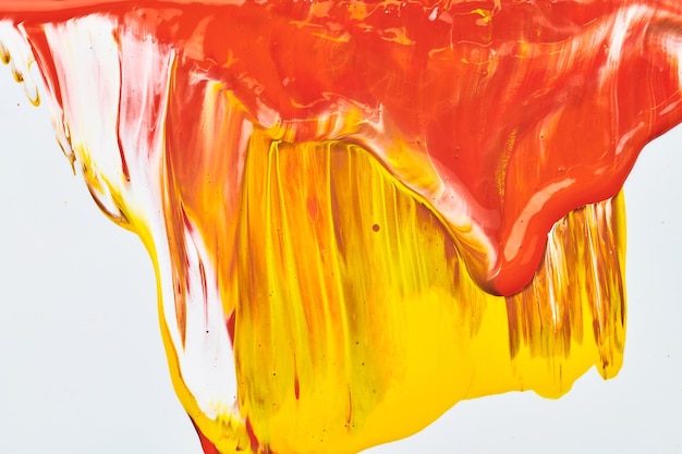 Chaotischer Pinselstrichfleck aus Acrylfarbe, der auf weißem Papierhintergrund fließt Kreative orangefarbene Hintergrundflüssigkeitskunst