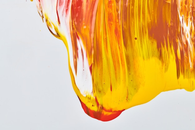 Chaotischer Pinselstrichfleck aus Acrylfarbe, der auf weißem Papierhintergrund fließt Kreative orangefarbene Hintergrundflüssigkeitskunst