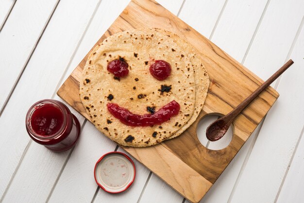 Chapati Roll con salsa de tomate o gelatina de mermelada de frutas con cara sonriente, menú de comida favorita de los niños indios para la escuela tiffin box, enfoque selectivo