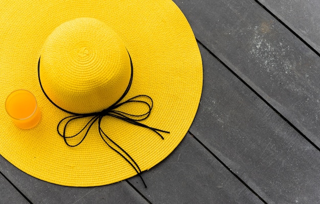 Foto chapéu amarelo com suco de laranja fresco na praia. férias de verão com espaço em fundo de madeira.