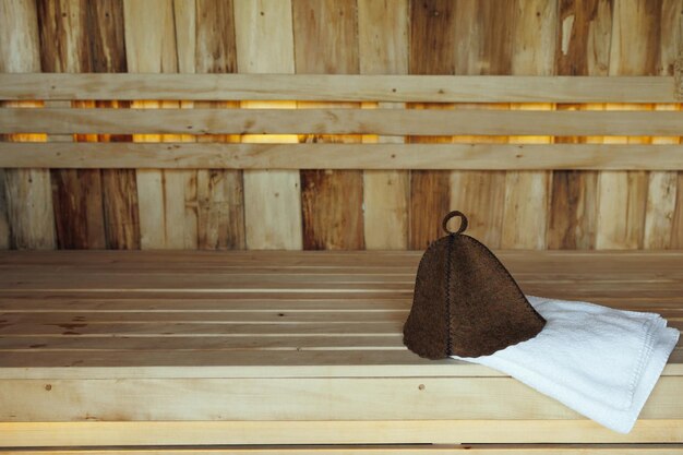 Chapéu de banho e toalha branca em tábuas de madeira na sauna