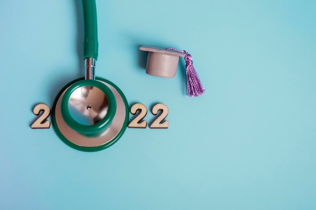 Chapéu de formatura com estetoscópio e números 2022 em fundo azul, close-up com espaço de cópia. Conceito de educação médica.