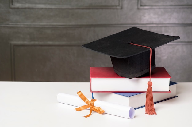 Chapéu de formatura com livros na mesa branca, fundo de educação