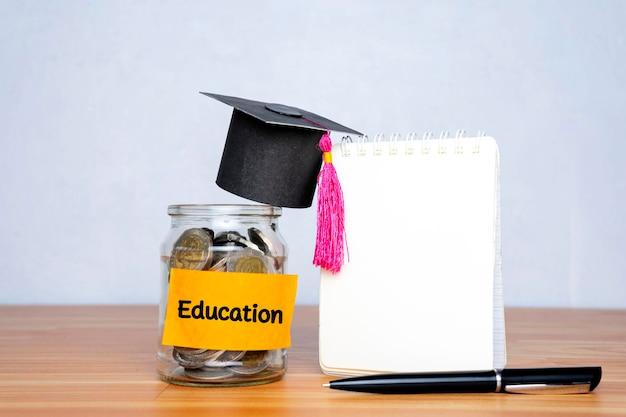 Chapéu de formatura e frasco de vidro com caneta de dinheiro e um caderno em branco para educação