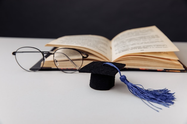 Chapéu de formatura e óculos com livro aberto sobre uma mesa. Conceito de educação.