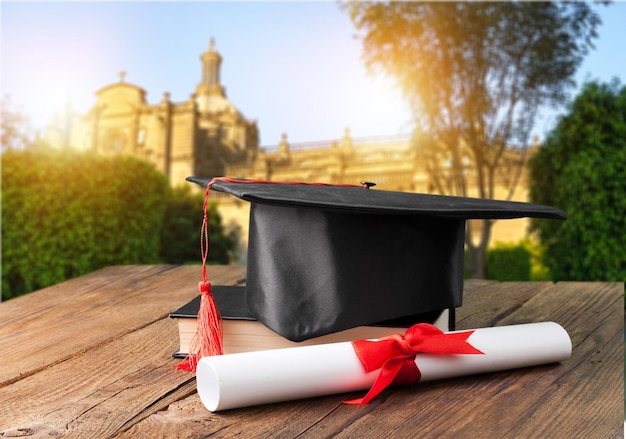 Chapéu de formatura, livro e diploma na mesa de madeira