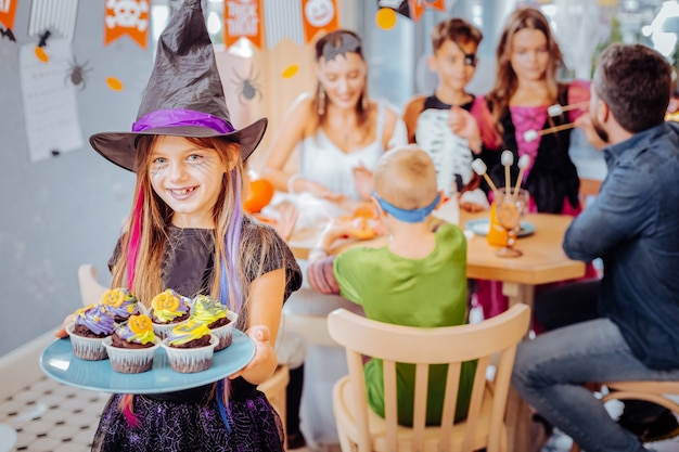 Chapéu de mago. Menina sorridente com chapéu de mago do Halloween segurando um prato com cupcakes de celebração por ocasião do aniversário