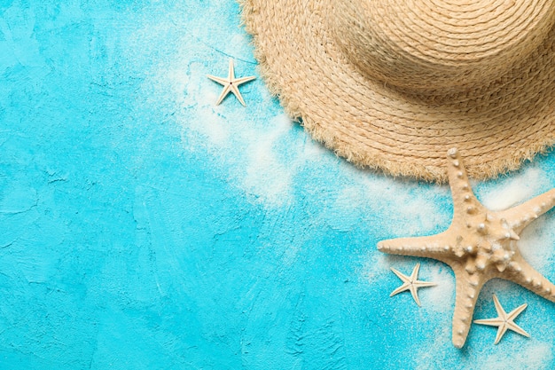 Chapéu de palha, areia e estrela do mar sobre fundo de cor, espaço para texto. Conceito de férias de verão