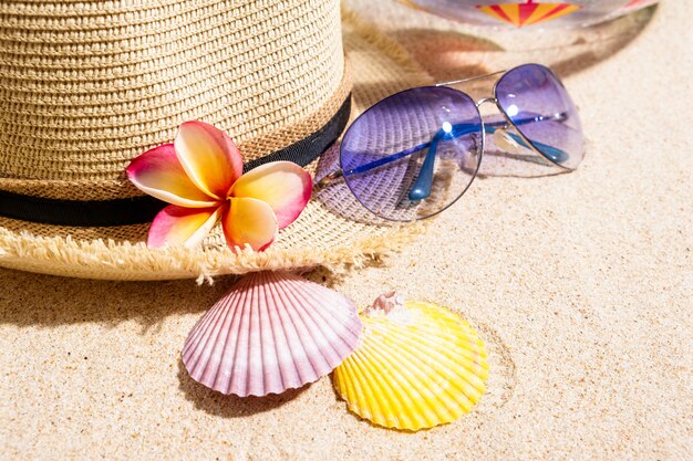 Foto chapéu de palha bege com óculos de sol azuis, conchas do mar colorido