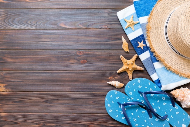 Chapéu de palha, chinelos azuis, toalha e estrela do mar em um fundo escuro de madeira. vista superior conceito de férias de verão com espaço de cópia.