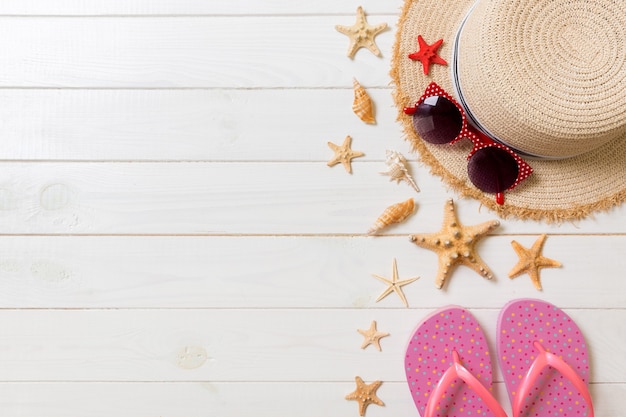 Chapéu de palha, chinelos rosa, óculos escuros e estrela do mar em um fundo branco de madeira. vista superior conceito de férias de verão com espaço de cópia.