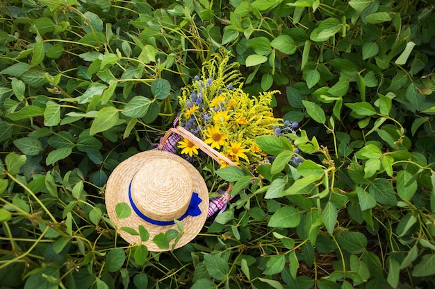 Chapéu de palha e cesta com flores ficam na grama