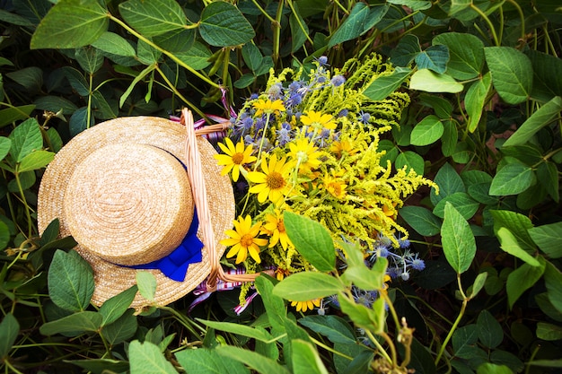 Chapéu de palha e cesta com flores ficar na grama, close-up