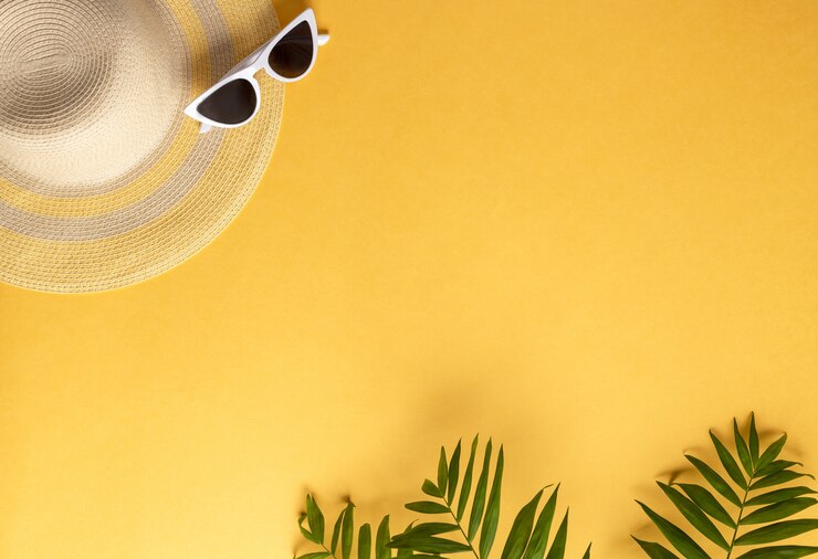 Chapéu de palha e óculos de sol em um fundo amarelo com folhas de palmeira Fundo horizontal de férias de verão, cópia espaço