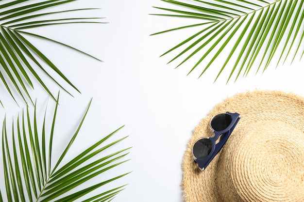 chapéu de palha, óculos de sol e folhas de palmeira em fundo branco