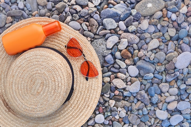 Chapéu de palha, óculos de sol laranja e uma garrafa de protetor solar para proteção solar durante o banho de sol. Copie o espaço