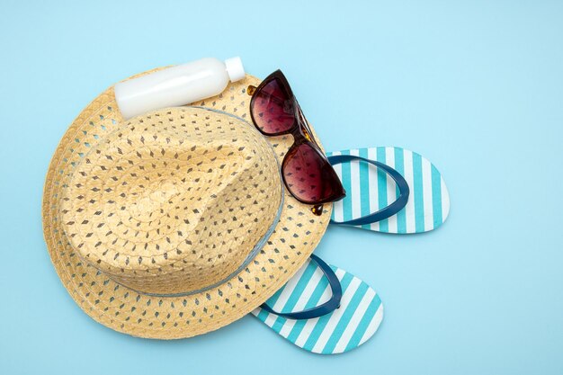 Foto chapéu de palha óculos de sol listrados chinelos creme solar em fundo azul fundo de verão