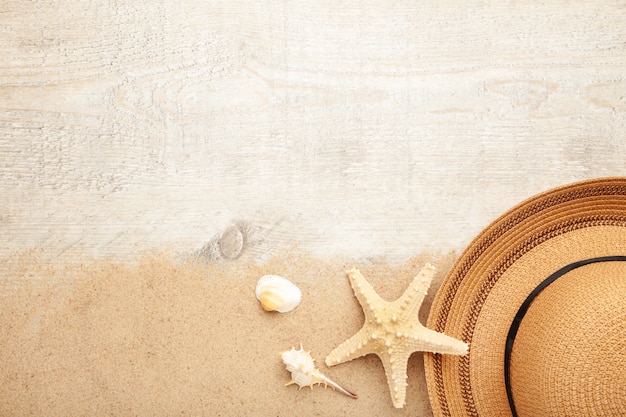 Chapéu de praia com conchas e areia na luz de fundo