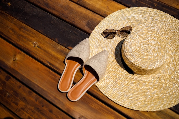 Chapéu de verão mulheres, óculos escuros e sapatos de mulas mentem sobre um fundo de madeira. Lugar para inscrição ou anúncio