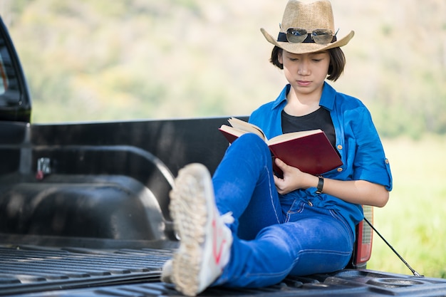 Chapéu do desgaste de mulher e lendo o livro na caminhonete