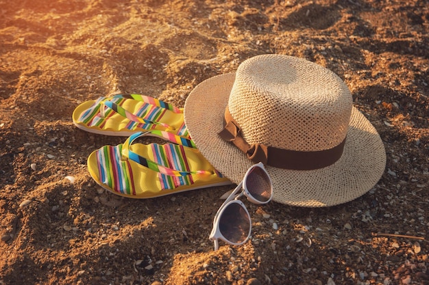 Chapéu e óculos de sol em chinelos coloridos de areia, você está pronto para passar as férias neste verão no resort