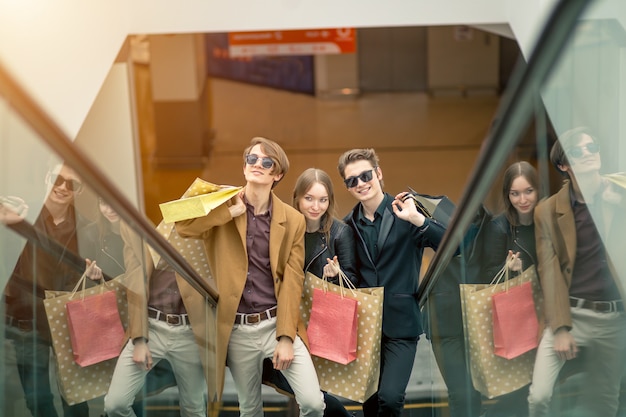 Chappy joven pareja con bolsas de compras bajando por las escaleras mecánicas y señalando con el dedo en el centro comercial