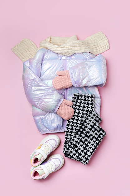 Chaqueta acolchada cálida para niños con pantalones y zapatillas sobre fondo rosa. Prendas de abrigo para niños con estilo. Traje de moda de invierno