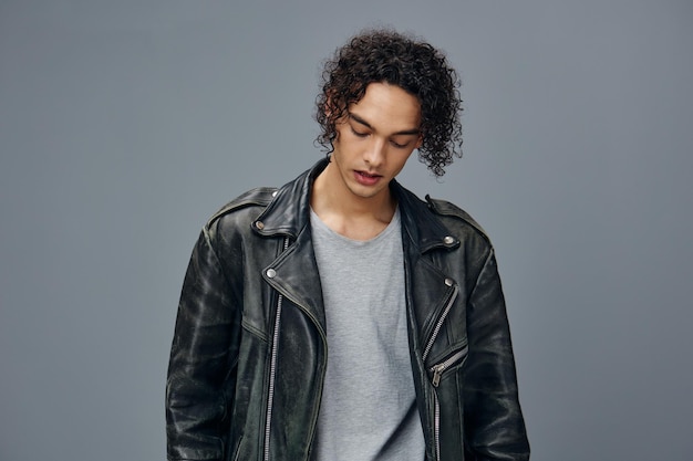 La chaqueta de cuero de hombre rizado bronceado con estilo adorable y serio se ve a un lado posando aislada sobre el fondo gris del estudio Oferta de moda fresca Gran venta de temporada Nuevo concepto de colección Copiar espacio para anuncios