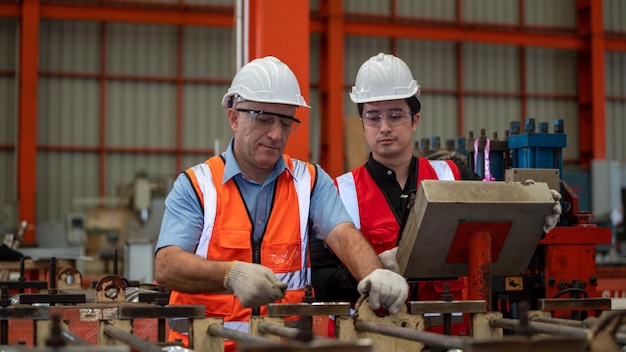 Chaqueta de seguridad de dos ingenieros de capataz de la industria pesada Máquina de verificación de mantenimiento preventivo diario en la fábrica de fabricación Uso de Labtop Discusión Capacitación Habilidades Calidad de mantenimiento