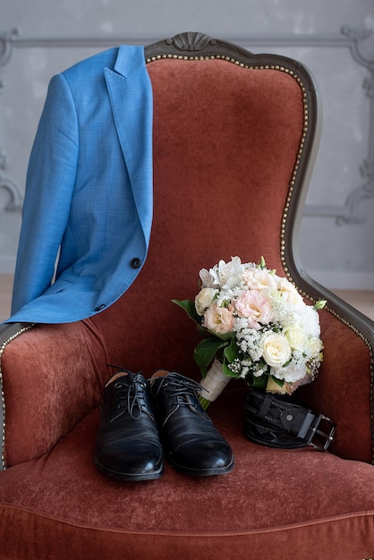 Foto chaqueta, zapatos, cinturón, ramo de flores en una silla, detalles de la boda matutina del novio.