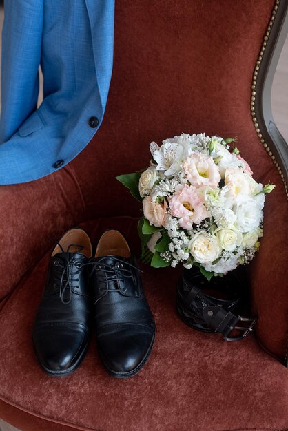 Foto chaqueta, zapatos, cinturón, ramo de flores en una silla, detalles de la boda matutina del novio.