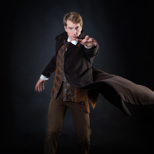 Charakter der Steampunk-Geschichte, junger attraktiver Mann in einem eleganten langen Mantel, Abenteurer macht eine epische Geste. intelligenter Gentleman im viktorianischen Stil. Vintage Retro-Anzug, junger attraktiver Mann