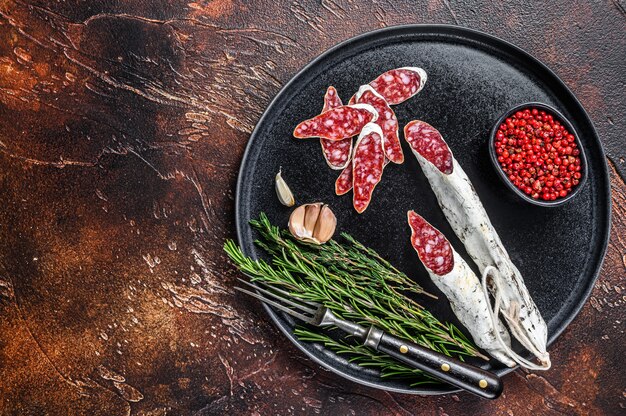 Charcuterie mit Fuet Salami Wurst und Rosmarin auf einem Teller auf Holztisch. Draufsicht.