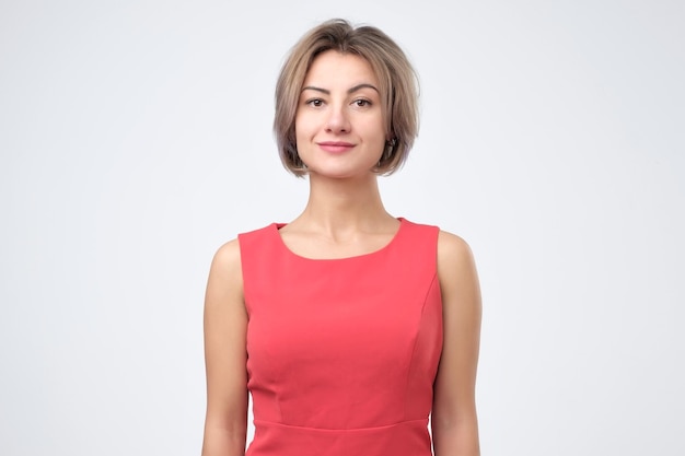 Charismatische, attraktive Frau im roten Kleid, die fröhlich lächelt, während sie vor grauem Hintergrund steht