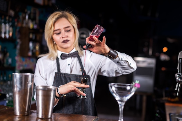 Charismatische Barkeeperin demonstriert den Prozess der Zubereitung eines Cocktails, während sie in der Kneipe in der Nähe der Bartheke steht