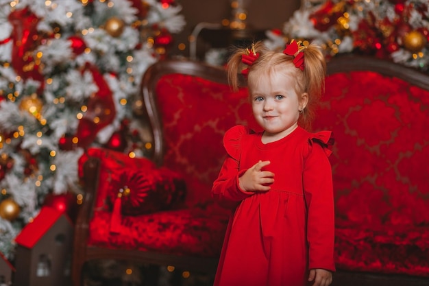 charismatisches kleines Mädchen in einem roten Kleid auf dem Hintergrund der Weihnachtsdekoration