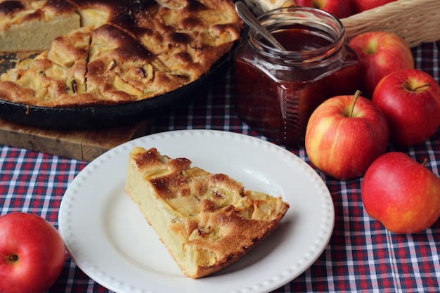 Charlotte, mermelada de fresa en tarro y manzanas en manteles rojos en una jaula.