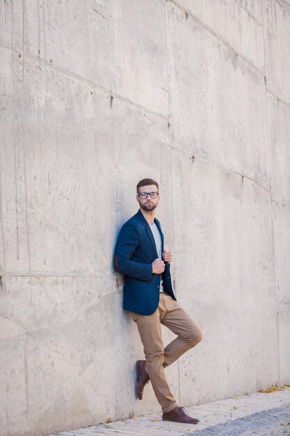 Charmant gutaussehend. Voller Länge eines gutaussehenden jungen Mannes in einer eleganten Jacke, der sich draußen an die Betonwand lehnt