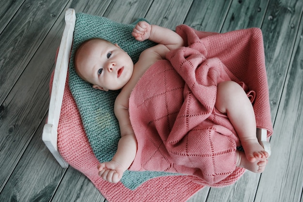 Charmant und süß ist ein Neugeborenes mit einer Strickdecke in einem handgefertigten Holzbett auf dem grünen Holzparkett bedeckt