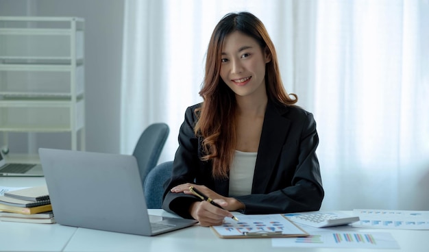 Charmante asiatische Frau, die im Büro mit einem Laptop arbeitet. Blick auf die KameraxA