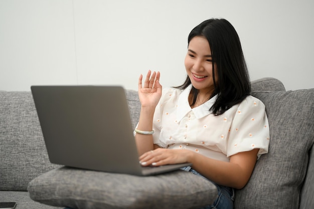 Charmante asiatische Frau entspannt auf dem Sofa sitzend mit Laptop-Computer für Videoanrufe mit ihrer Familie